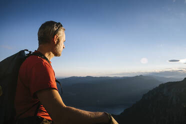 Älterer Mann mit Rucksack, der bei Sonnenuntergang die Berge gegen den Himmel betrachtet, Orobie, Lecco, Italien - MCVF00455