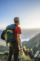 Wanderer mit Rucksack, der bei Sonnenuntergang die Berge gegen den klaren Himmel betrachtet, Orobie, Lecco, Italien - MCVF00456