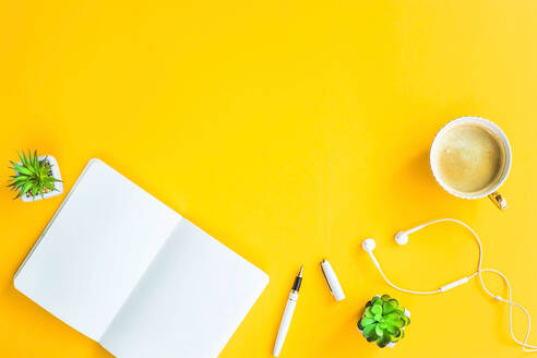 Direkt über Schuss von Kaffee mit Buch und In-Ear-Kopfhörer auf gelbem Tisch - EYF07037