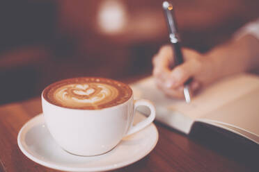 Cropped Hand der Frau Schreiben auf Buch von Kaffee auf dem Tisch - EYF07038