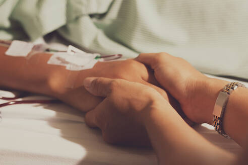 Close-Up Of Woman Holding Patient Hand Lying On Bed At Hospital - EYF07065