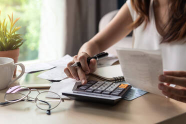 Midsection Of Woman Using Calculator On Table At Home - EYF07091