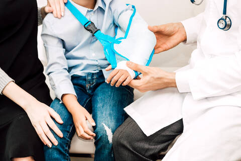 Mittelteil eines Arztes, der einen Jungen mit gebrochenem Arm im Krankenhaus untersucht, lizenzfreies Stockfoto