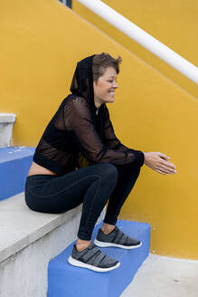 Lächelnde, sportliche Frau auf einer Treppe sitzend - LVVF00083