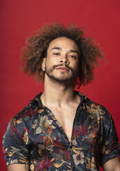 Handsome young man with curly hair standing against red background - SNF00348