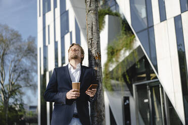 Businessman with takeaway coffee and smartphone in the city - JOSEF00879