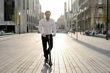 Businessman riding kick scooter in the city - JOSEF00890