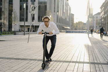 Businessman riding kick scooter in the city - JOSEF00891