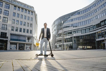 Geschäftsmann mit Kick-Scooter und Blumenstrauß in der Stadt - JOSEF00907