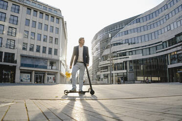 Geschäftsmann mit Kick-Scooter und Blumenstrauß in der Stadt - JOSEF00908