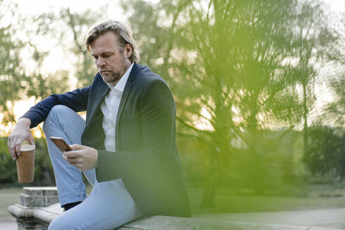 Geschäftsmann mit Kaffee zum Mitnehmen und Smartphone im Stadtpark - JOSEF00932