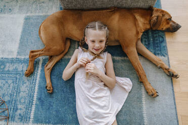 Niedliches Mädchen mit braunem Hund liegt auf Teppich zu Hause - OGF00450