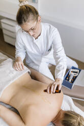 Cupping therapy, female alternative practitioner applying oil for treatment at back - DAWF01693