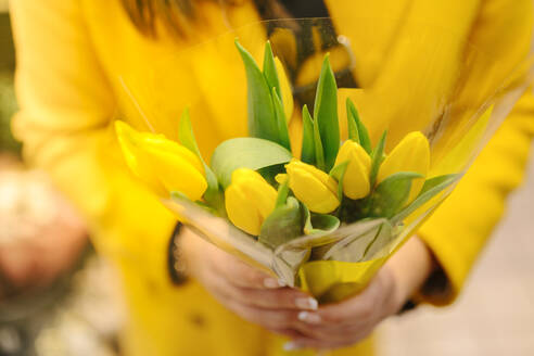 Unrecognizable woman with a bouquet of yellow tulips. She just receive - CAVF85552