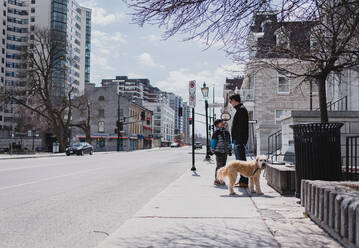 Vater und Sohn mit Hund stehen auf dem Bürgersteig einer ruhigen Stadtstraße. - CAVF85558