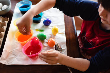 Close up of boy dipping an egg into dye to color it for Easter. - CAVF85566