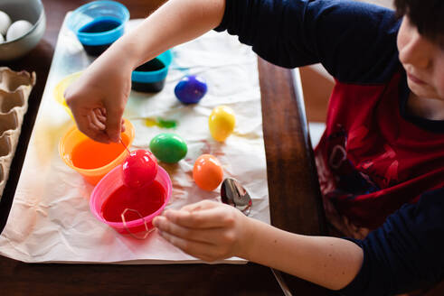 Nahaufnahme eines Jungen, der ein Ei in Farbe taucht, um es für Ostern zu färben. - CAVF85566