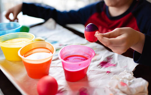 Nahaufnahme eines Jungen, der ein Ei in Farbe taucht, um es für Ostern zu färben. - CAVF85567