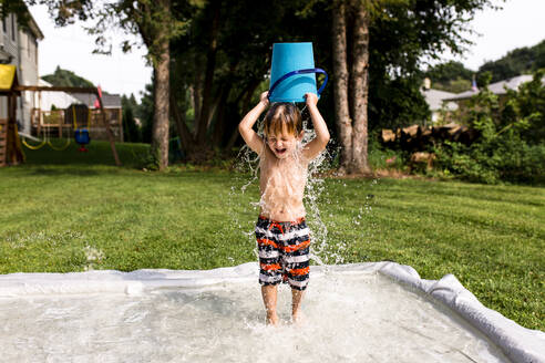 Junger Junge gießt Wasser Eimer über Kopf - CAVF85626