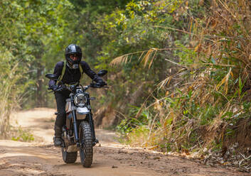 Frau fährt mit ihrem Scrambler-Motorrad durch den Wald - CAVF85629