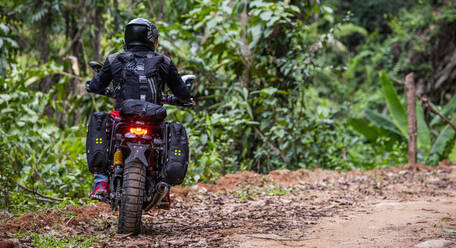 Frau fährt mit ihrem Scrambler-Motorrad durch den Wald - CAVF85635