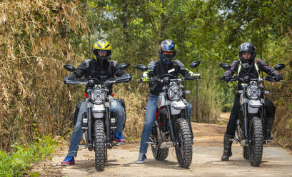 Three friends riding their scrambler motorcycles through forrest - CAVF85641