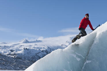 Frau klettert auf einen Eisberg in der Lagune des Fjallsjoull-Gletschers - CAVF85644