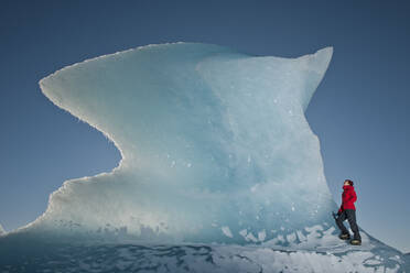 Frau klettert auf einen Eisberg in der Lagune des Fjallsjoull-Gletschers - CAVF85645