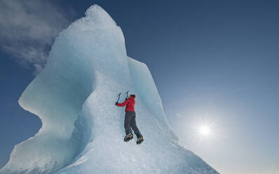 Frau klettert auf einen Eisberg in der Lagune des Fjallsjoull-Gletschers - CAVF85646