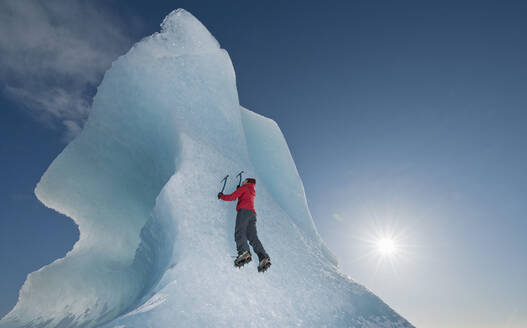 Frau klettert auf einen Eisberg in der Lagune des Fjallsjoull-Gletschers - CAVF85646