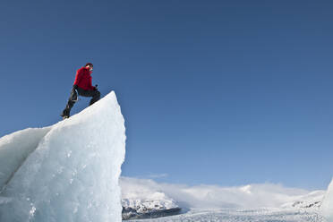 Frau klettert auf einen Eisberg in der Lagune des Fjallsjoull-Gletschers - CAVF85647