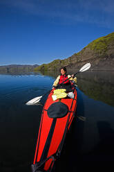 Woman rowing sea kayak on still lake in central Iceland - CAVF85721