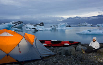 Woman using her laptop at campsite by glacier lagoon - CAVF85735