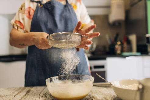 Nahaufnahme einer Bäckerin beim Sieben von Mehl in Teig auf einem Tisch in einer Werkstatt - GMLF00240