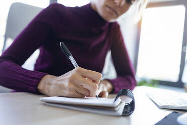 Nahaufnahme einer Geschäftsfrau, die im Büro sitzend auf einen Notizblock schreibt - JSRF00969