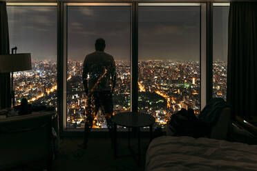 Japan, Präfektur Osaka, Osaka, Silhouette eines Mannes, der durch ein Hotelfenster in der nächtlichen Stadt schaut - EHF00345