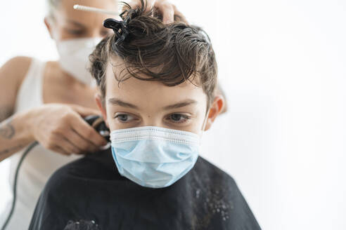 Close-up of hairdresser cutting boy's hair wearing mask at home during curfew - SNF00368