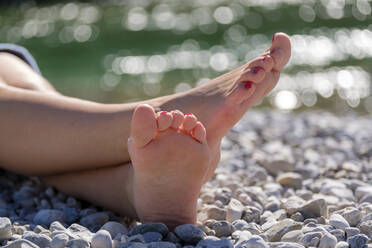 Junge Frau mit Barfuß auf Kieselsteinen am Flussufer sitzend - LBF03074