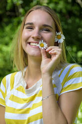 Nahaufnahme einer lächelnden schönen Frau, die Gänseblümchen im Park hält - LBF03078