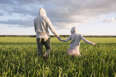 Father and daughter holding hands while walking amidst plants on landscape - EYAF01156