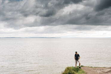 Mann steht auf einer Klippe und blickt auf das Meer vor Gewitterwolken - JVSF00018