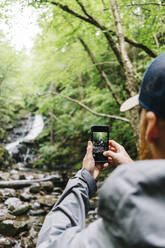 Mann fotografiert Wasserfall beim Wandern im Wald - JVSF00020