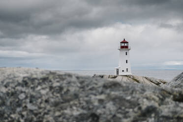 Peggys Point Lighthouse on rock formation by sea against cloudy sky, Nova Scotia, Canada - JVSF00023