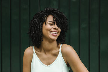 Cheerful young woman with eyes closed standing against metal door - XLGF00226