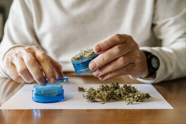 Midsection of senior man grinding weed in grinder at home - AFVF06692