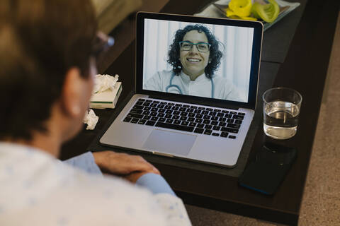 Lächelnder Arzt bei einem Videogespräch mit einer kranken älteren Frau über einen Laptop, lizenzfreies Stockfoto