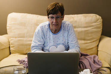 Retired senior woman discussing illness with doctor over video call through laptop at home - XLGF00236