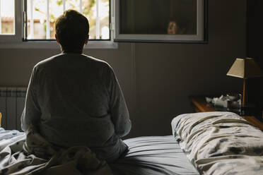 Retired elderly woman sitting on bed at home - XLGF00241