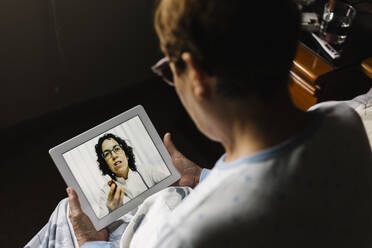 Ältere Frau bespricht sich per Videoanruf über ein digitales Tablet mit einem Arzt im Schlafzimmer - XLGF00245