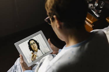 Elderly woman discussing over video call through digital tablet with doctor in bedroom - XLGF00245